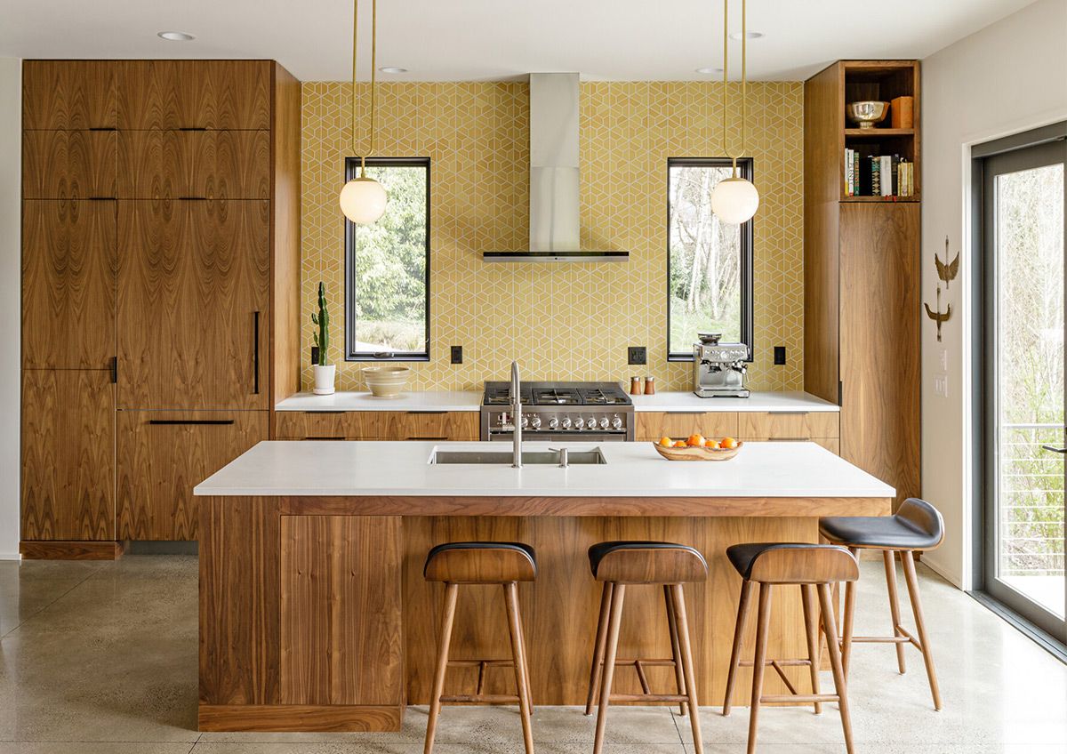 A kitchen with wooden cabinets and white counter tops, along with an island in the middle of the middle of the room with wood flooring and white cabinets and white counter tops is lit by recessed lighting hanging from